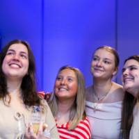 Grads smile and take selfie holding glasses